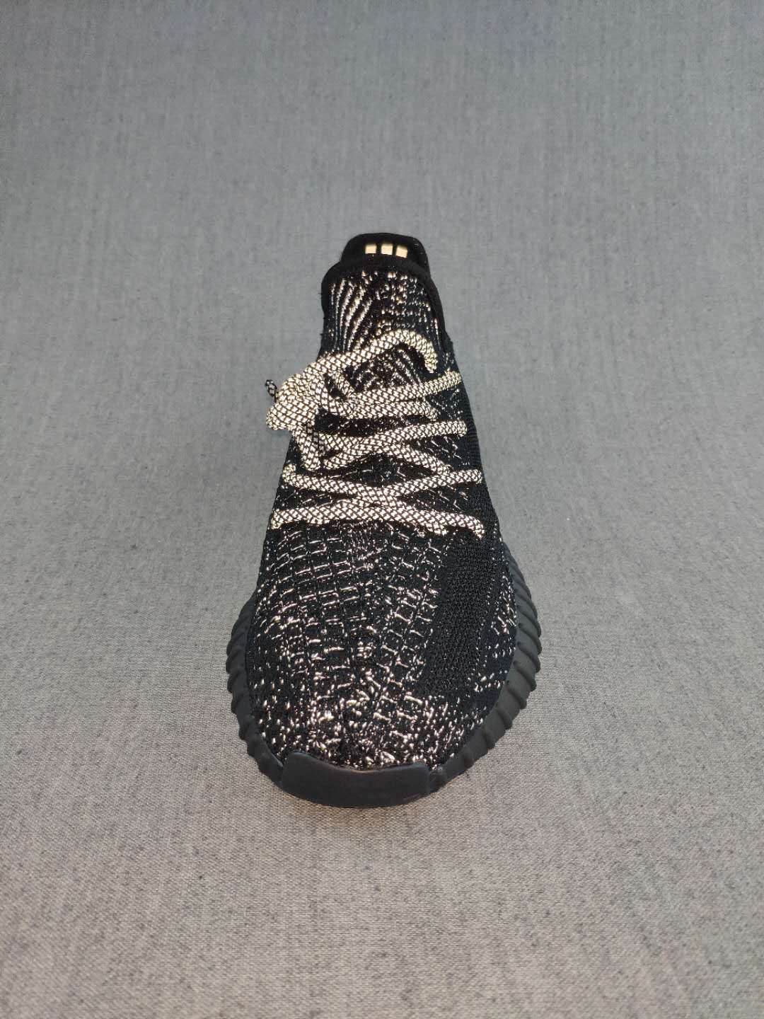 Front view of a black sneaker showing the rounded toe, light-colored laces, and textured speckled upper.