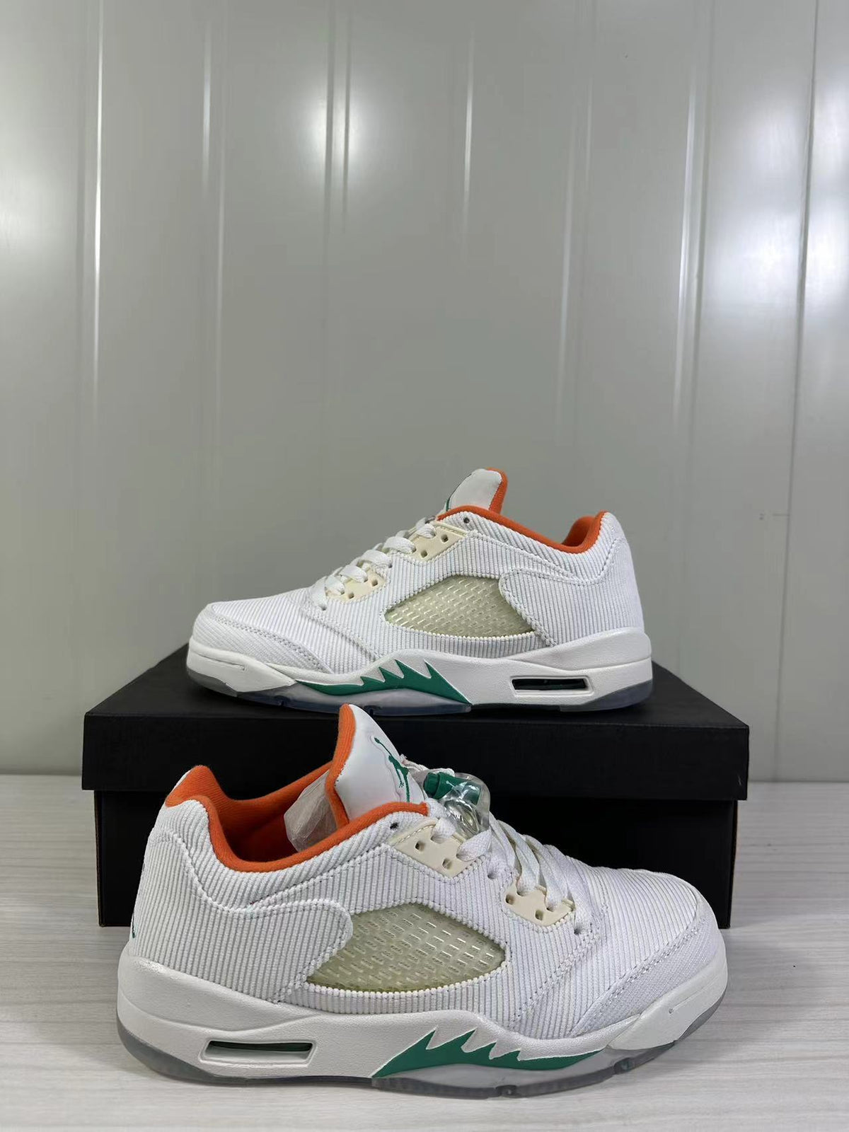 Pair of white low-top Jordan sneakers with green midsole accents, orange lining, and translucent side panels.