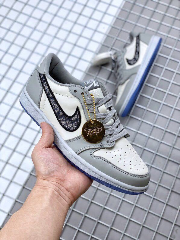 Front three-quarter view showing grey laces, white perforated toe panel, patterned Swoosh, and a round gold-tone hangtag.