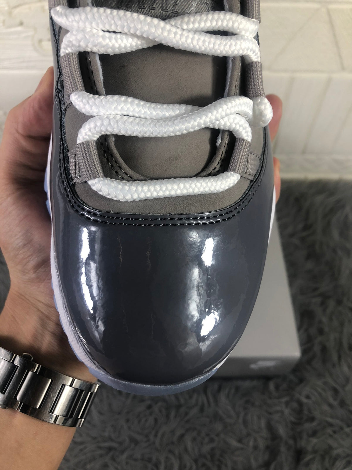 Close-up of the glossy dark toe panel, white laces, and grey upper.