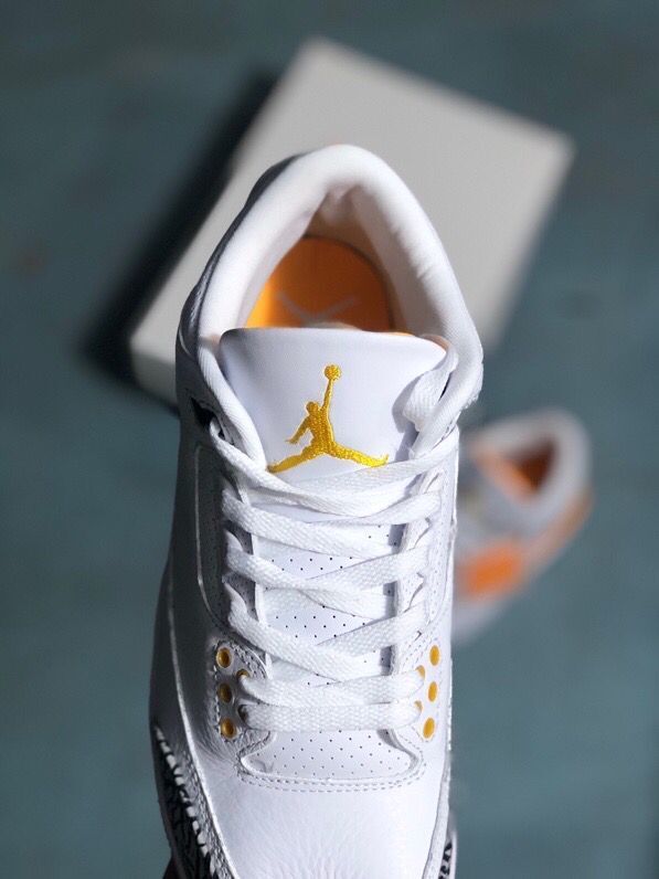 Close-up of the white sneaker tongue with gold Jumpman-style logo and orange eyelets.
