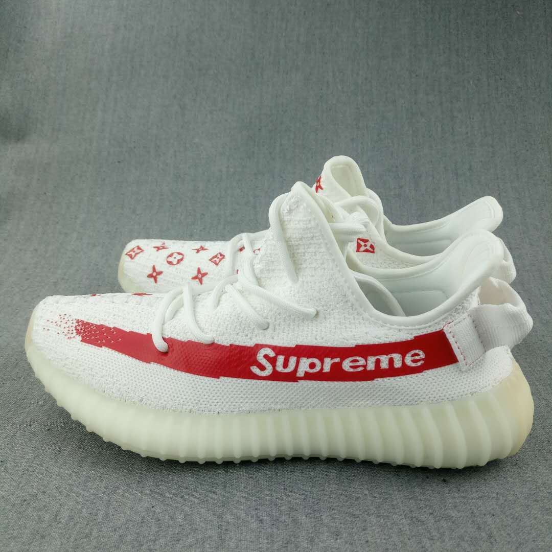 Side view of multiple white sneakers showing the red stripe, printed motifs, rear pull tabs, and ribbed soles.