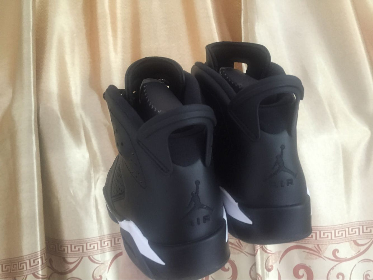 Rear view of the sneakers against a curtain, showing dark heel branding and white midsole accents.