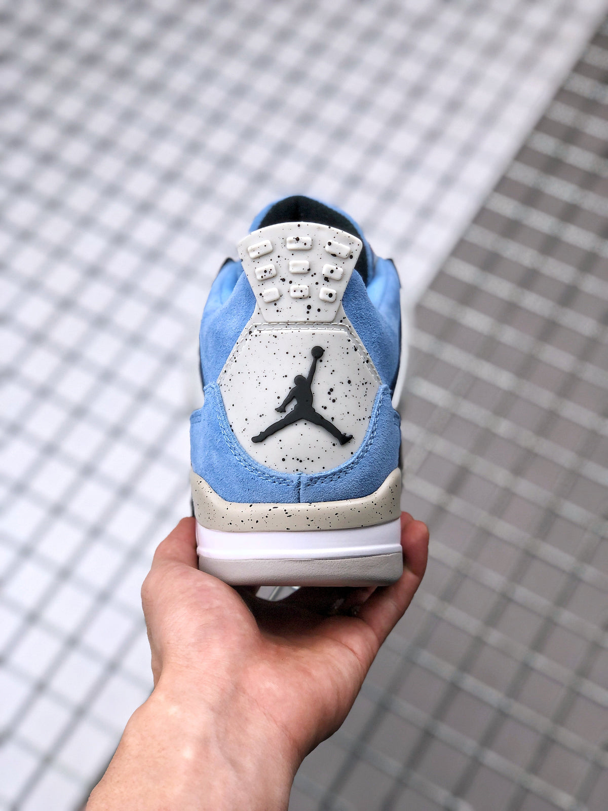 Rear view of a blue Air Jordan 4 sneaker showing the heel branding and speckled heel panel.
