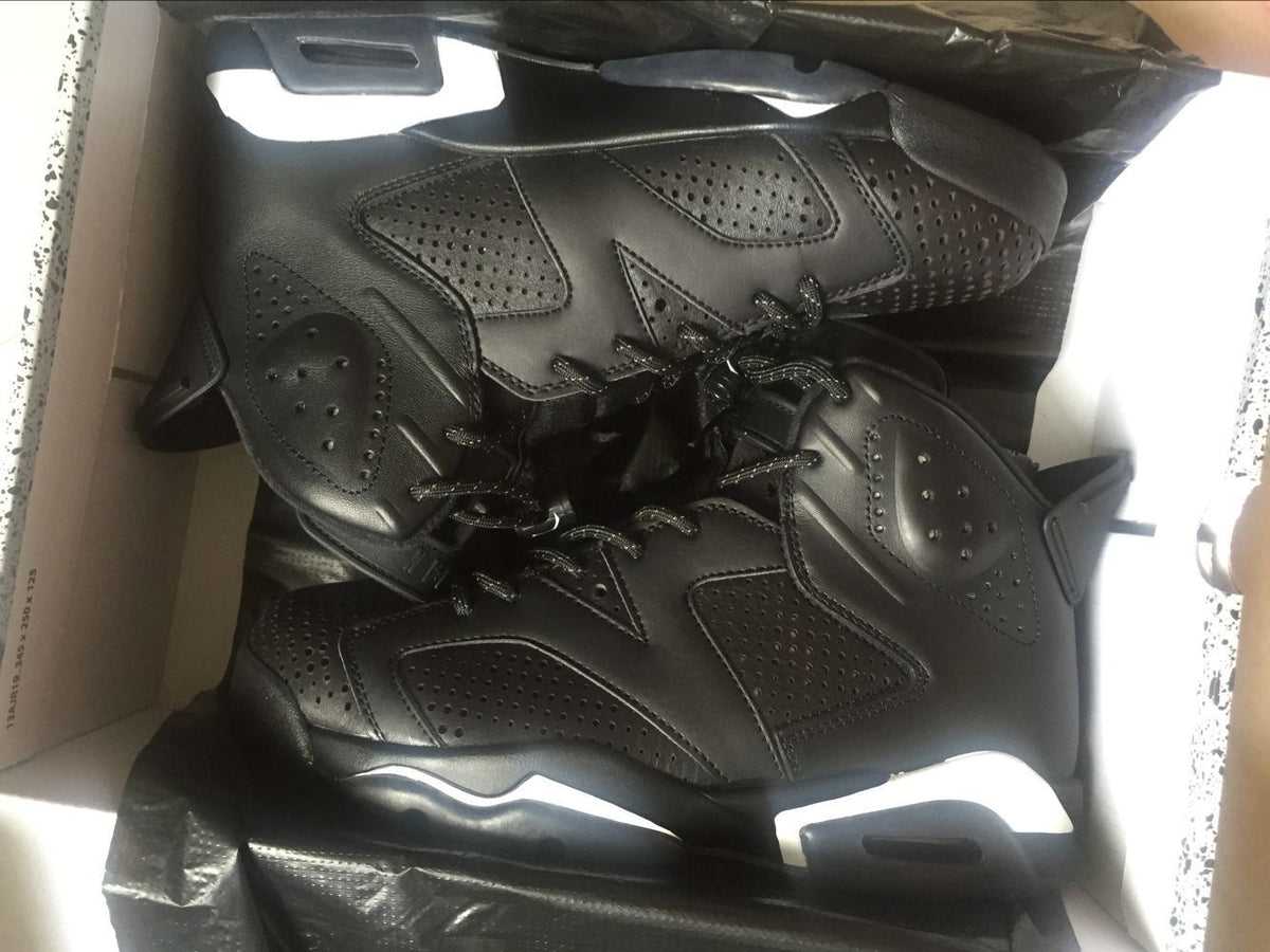 Top-down view of the black sneakers in a box, highlighting perforated upper panels and layered construction.
