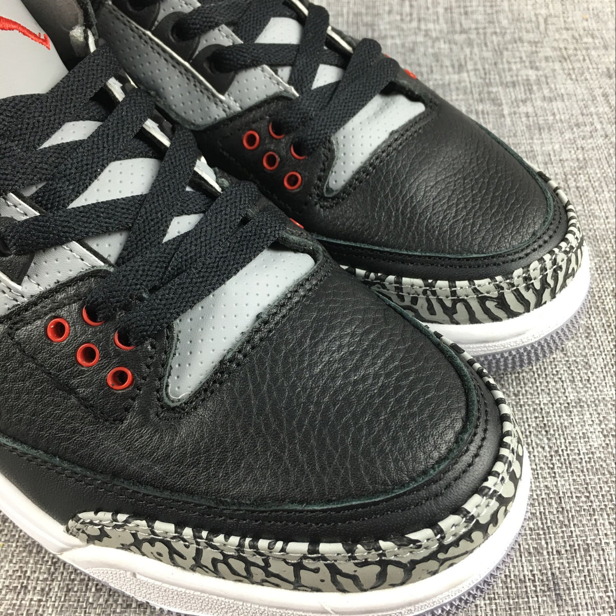 Close-up of black toe panels, grey perforated lace panels, red eyelets, and elephant-print trim