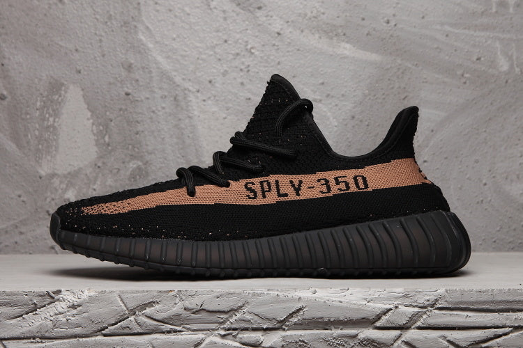 Side profile of a black Yeezy 350 V2-style sneaker with a peach-toned stripe, SPLY-350 lettering, and ribbed outsole.
