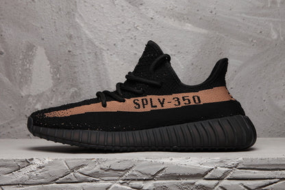 Side profile of a black Yeezy 350 V2-style sneaker with a peach-toned stripe, SPLY-350 lettering, and ribbed outsole.