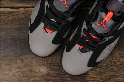 Close-up view of a black and grey pair of high-top sneakers with red tongue accents on a wooden surface.