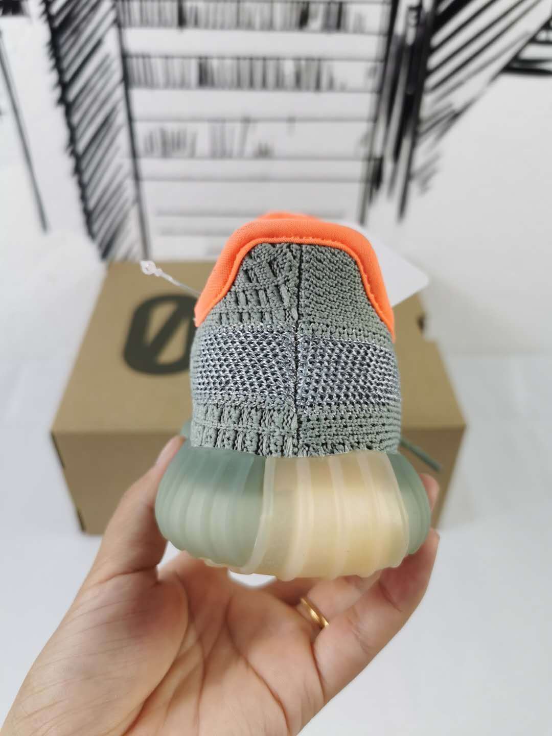 Rear view of the gray sneaker held by hand, highlighting the heel and translucent sole.