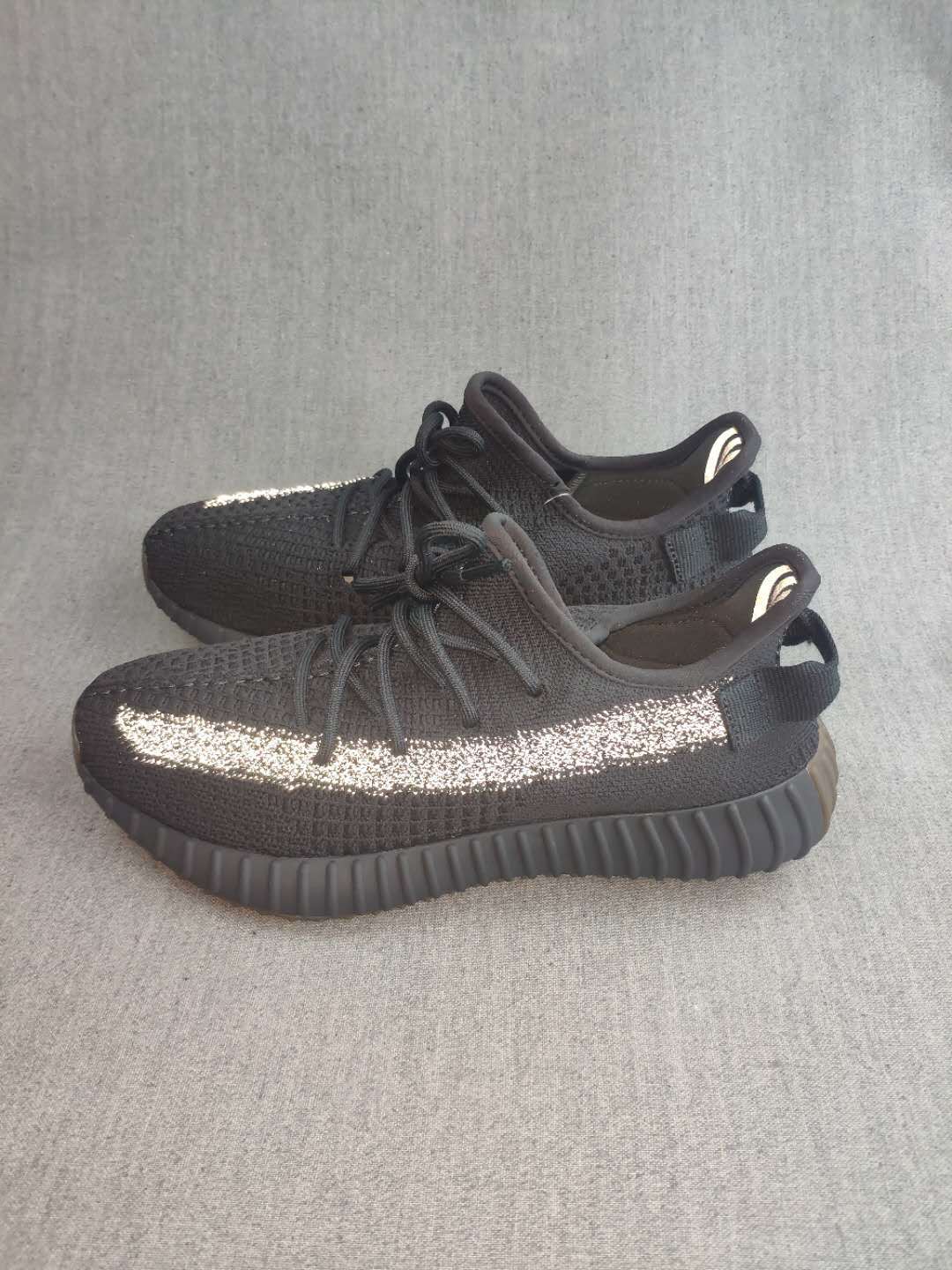 Pair of black Yeezy 350 V2-style sneakers shown from the side, featuring reflective side stripes and ribbed outsoles.