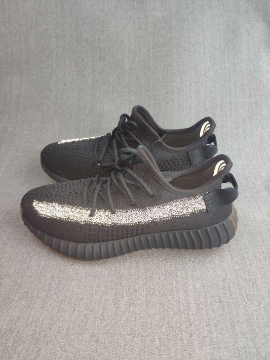 Pair of black Yeezy 350 V2-style sneakers shown from the side, featuring reflective side stripes and ribbed outsoles.