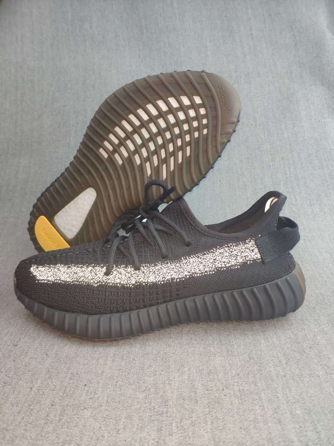 Black sneaker shown from the side with the outsole facing upward, revealing the ribbed sole pattern and contrasting heel insert.