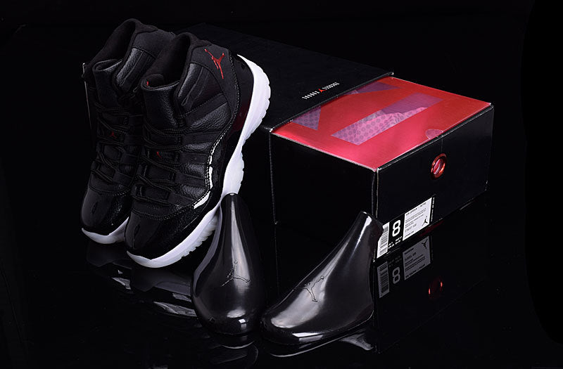 Pair of black high-top sneakers beside a black and red shoebox, viewed from above with glossy black accessories.
