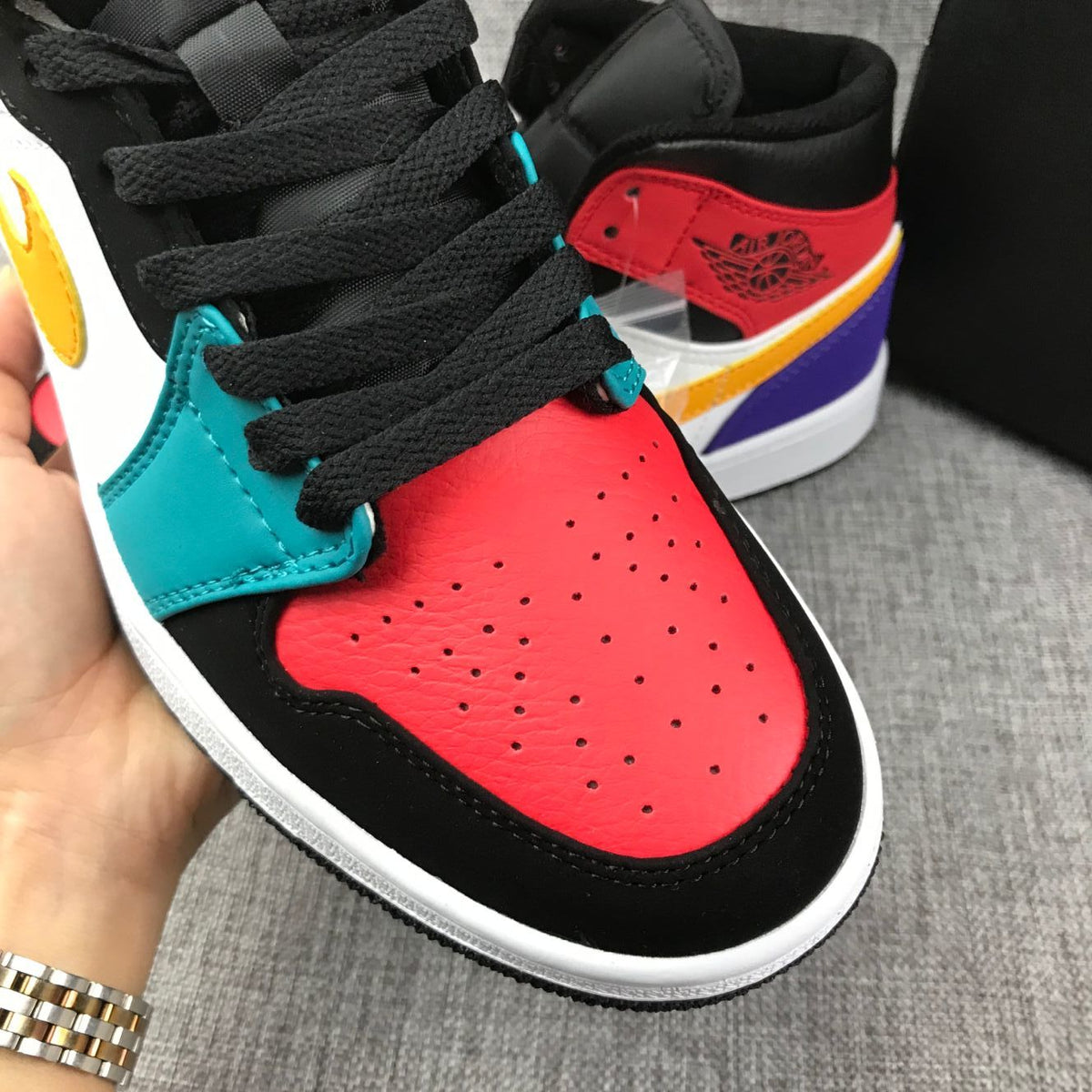 Close-up of the red perforated toe box with black laces and teal eyelet panels.
