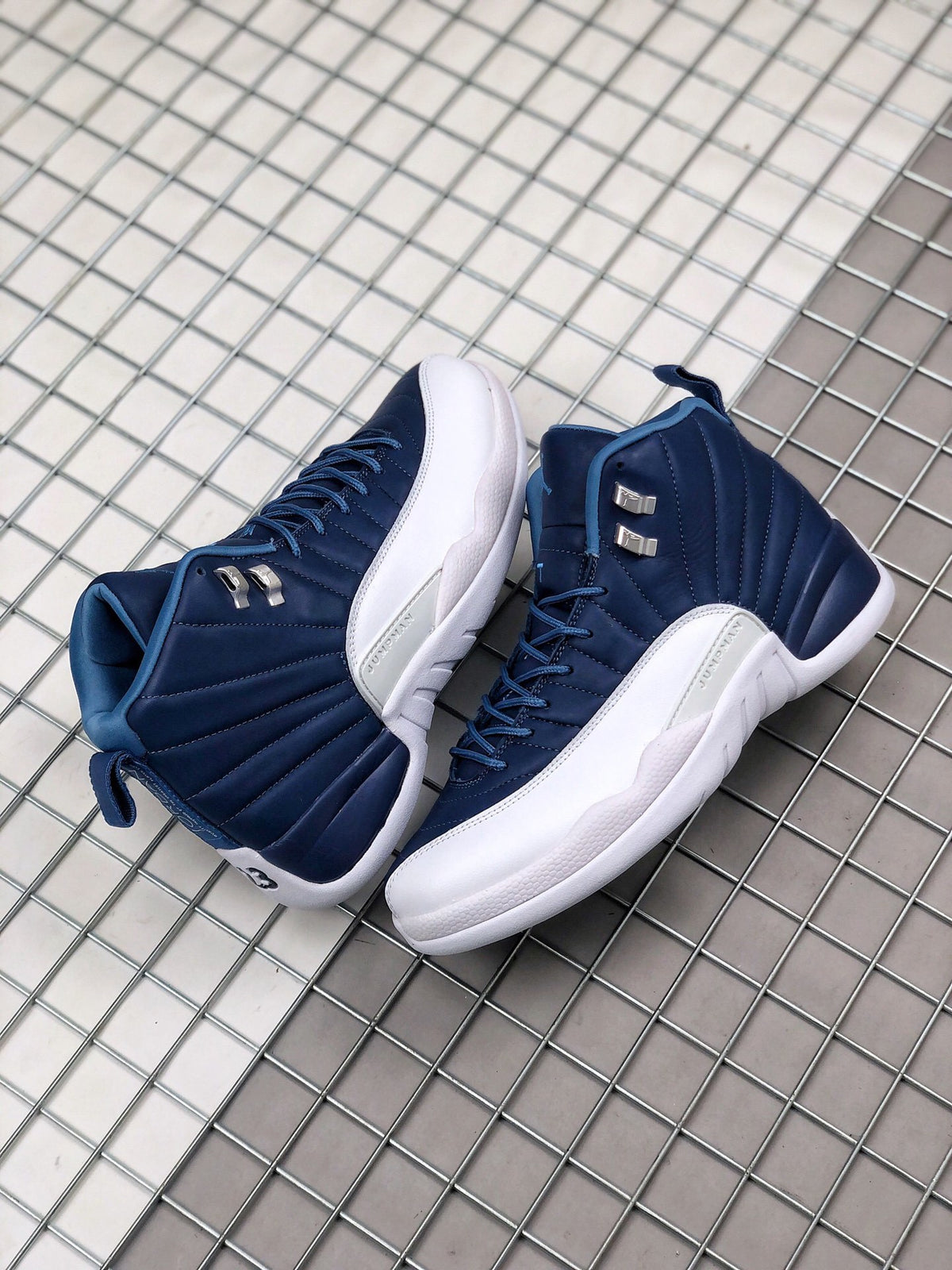 Pair of indigo and white high-top Jordan sneakers displayed on a metal grid surface.
