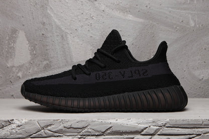 Side profile of a black Yeezy 350 V2 sneaker showing the tonal side stripe and ribbed sole.