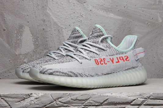 Side view of a gray and white Yeezy 350 V2 sneaker with red side lettering, mint collar accents, and a translucent ribbed sole.
