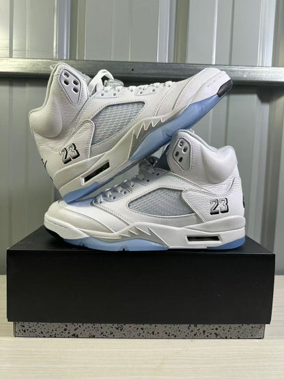 Two white and silver high-top sneakers arranged on a black shoe box from an angled side view.