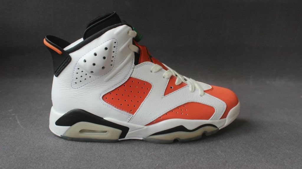Profile view of the sneaker showing the perforated orange panels, white overlays, black heel accents, and translucent midsole section.