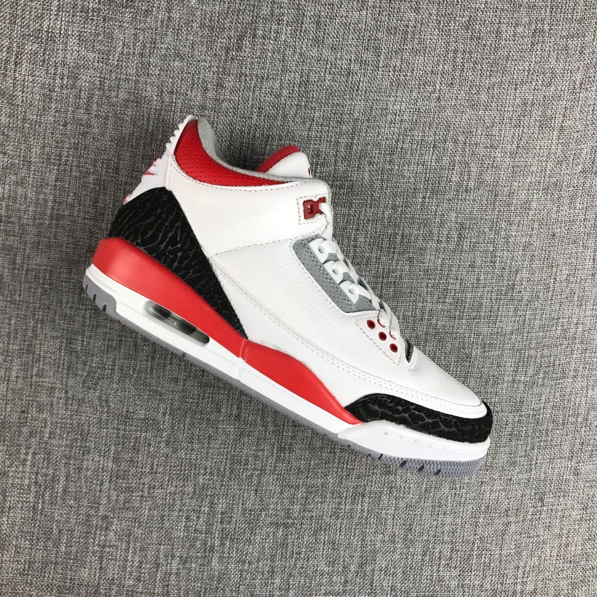 Angled view showing the white upper, gray lace panel, red accents, and black textured overlays.