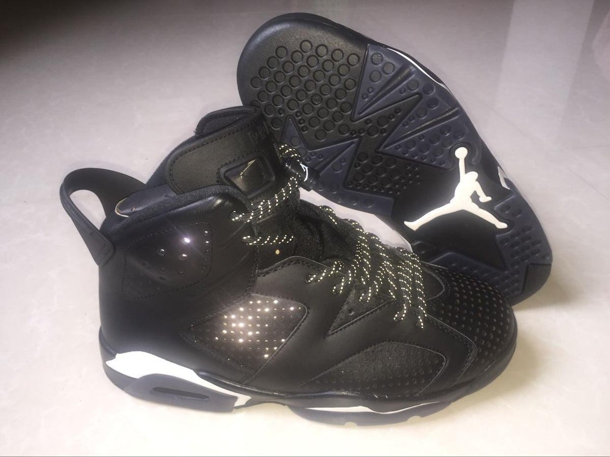Side view of a black Jordan 6 sneaker beside its outsole, showing the high-top shape and circular traction pattern.