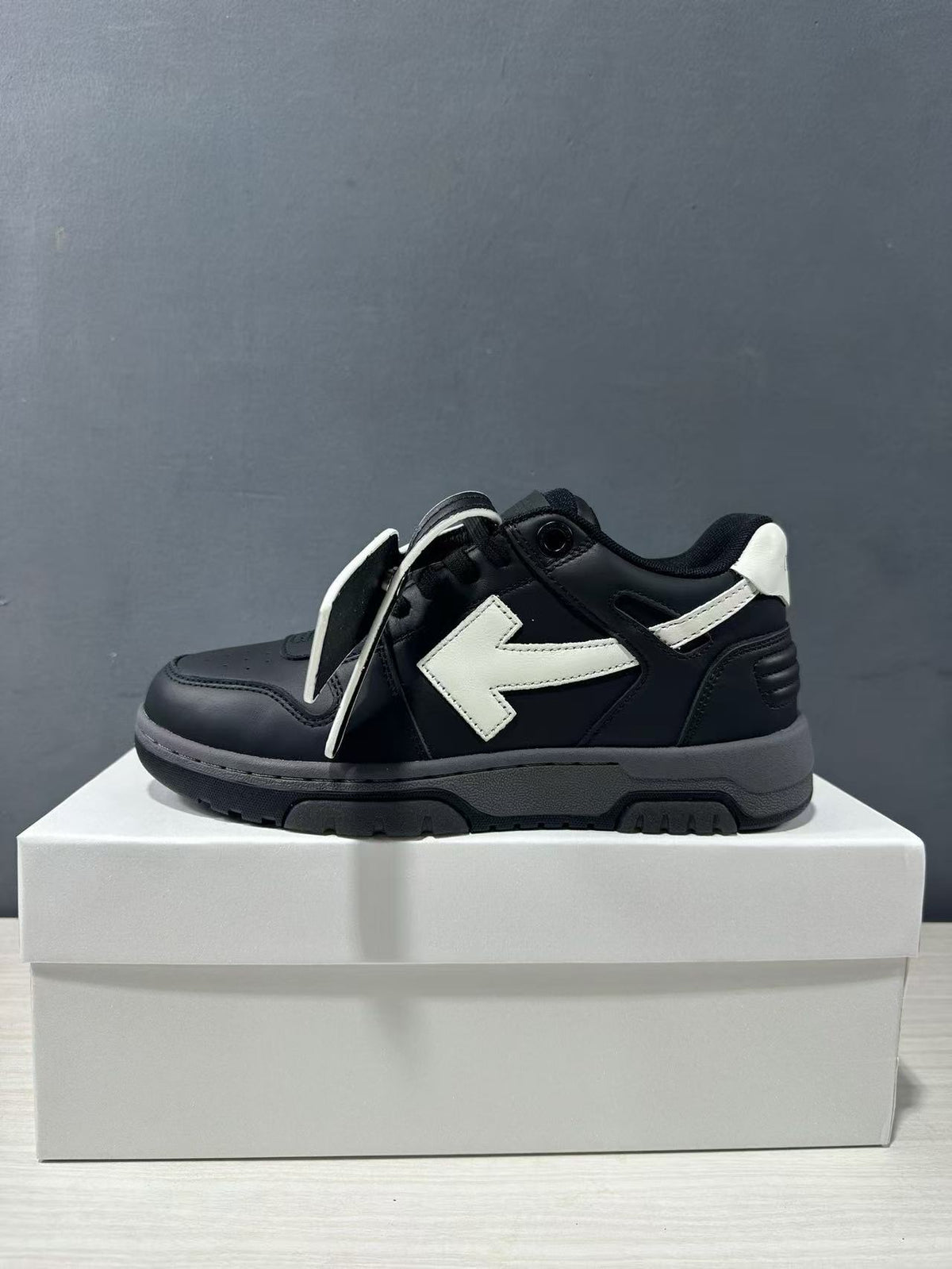Side profile of a black sneaker with white arrow detail and loose laces.