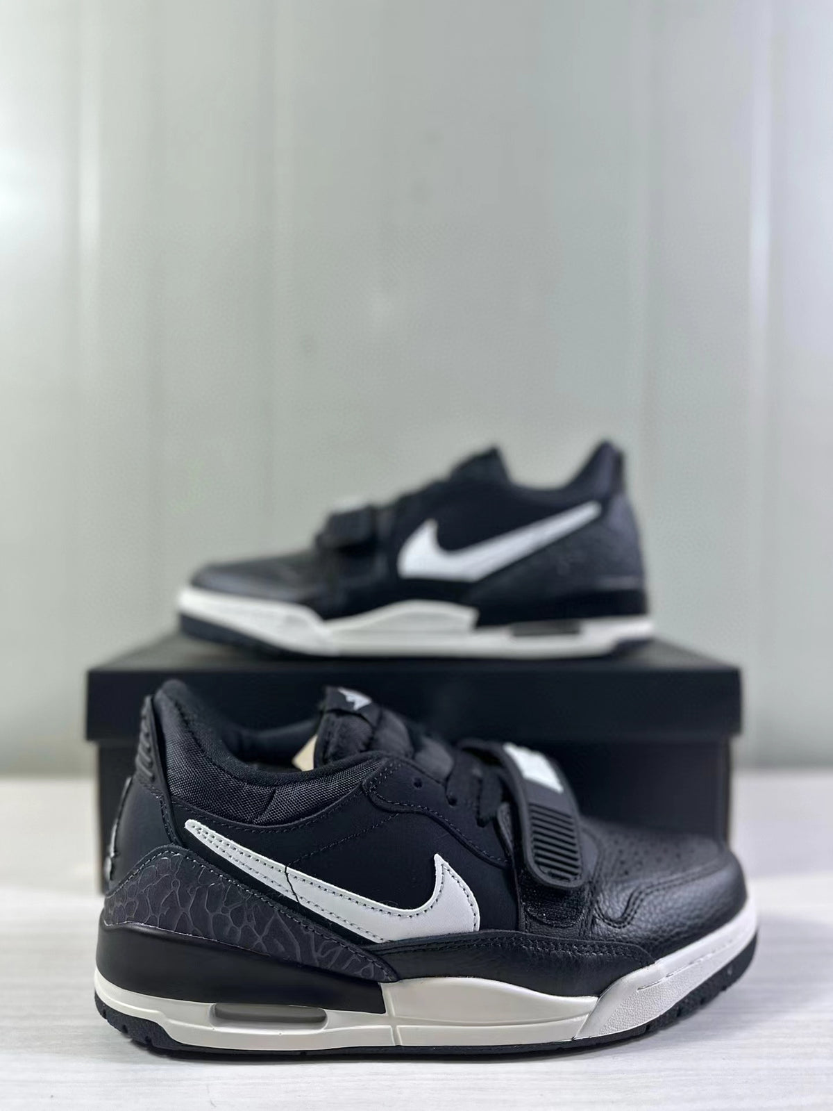 Angled side view highlighting the white side detailing, textured heel panel, strap, and layered black and white midsole.