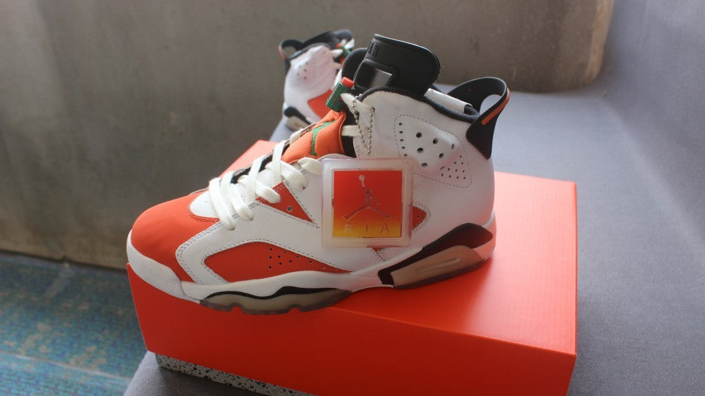 Side view of one white, orange, and black high-top sneaker resting on the orange shoe box.
