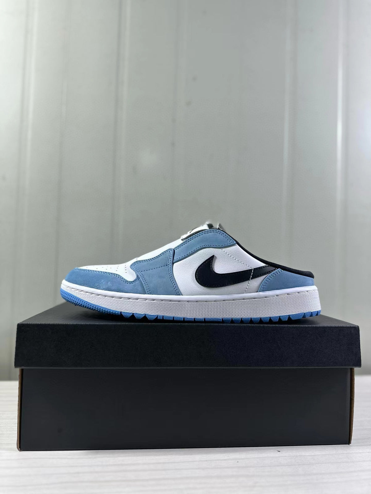 Single mule sneaker shown in side profile with a blue outsole and black side logo.