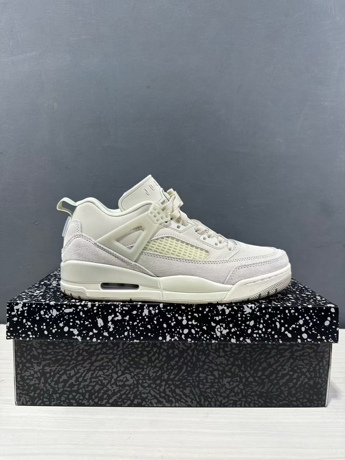 Side profile of white and light grey Jordan Spizike sneakers displayed on a patterned shoebox.