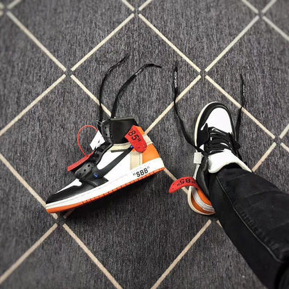 Angled view of the sneaker pair showing black laces, white toe panels, and orange accents.