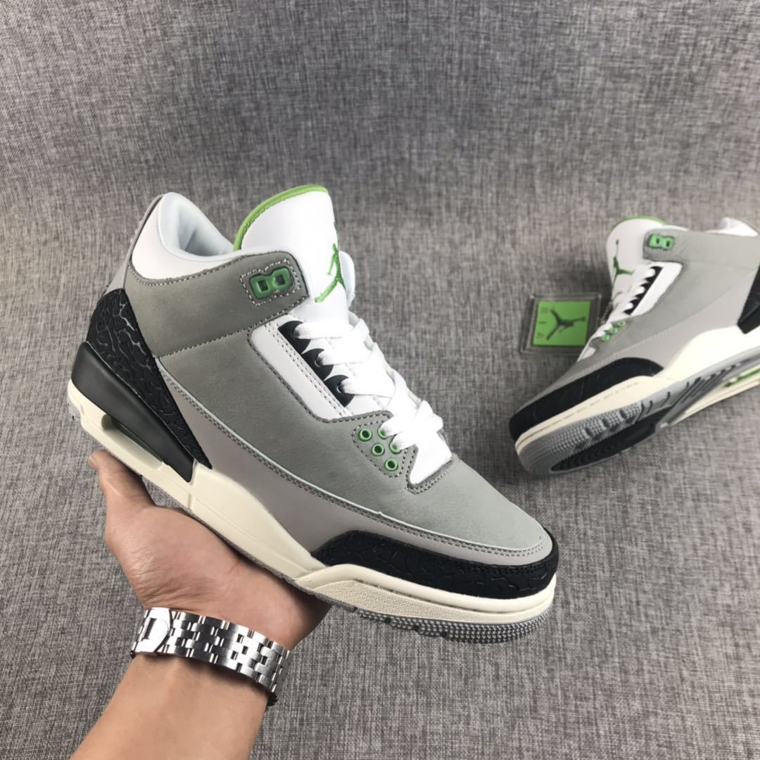 Handheld three-quarter view of a gray Air Jordan 3 sneaker with black, white, and green accents.