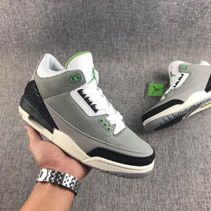 Handheld three-quarter view of a gray Air Jordan 3 sneaker with black, white, and green accents.