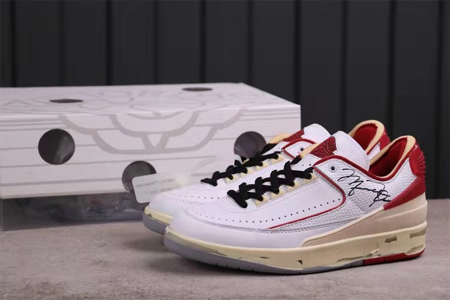 Pair of white and red low-top sneakers displayed in front of a shoebox.