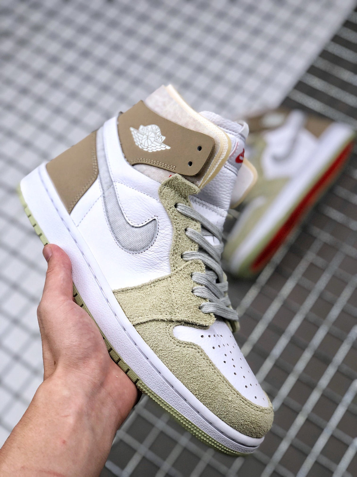 Three-quarter view of the sneaker showing the white perforated toe box, olive green overlays, gray laces, and brown ankle panel.
