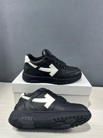 Pair of black and white low-top sneakers shown from the side and outsole, highlighting the white arrow detail and textured black tread.