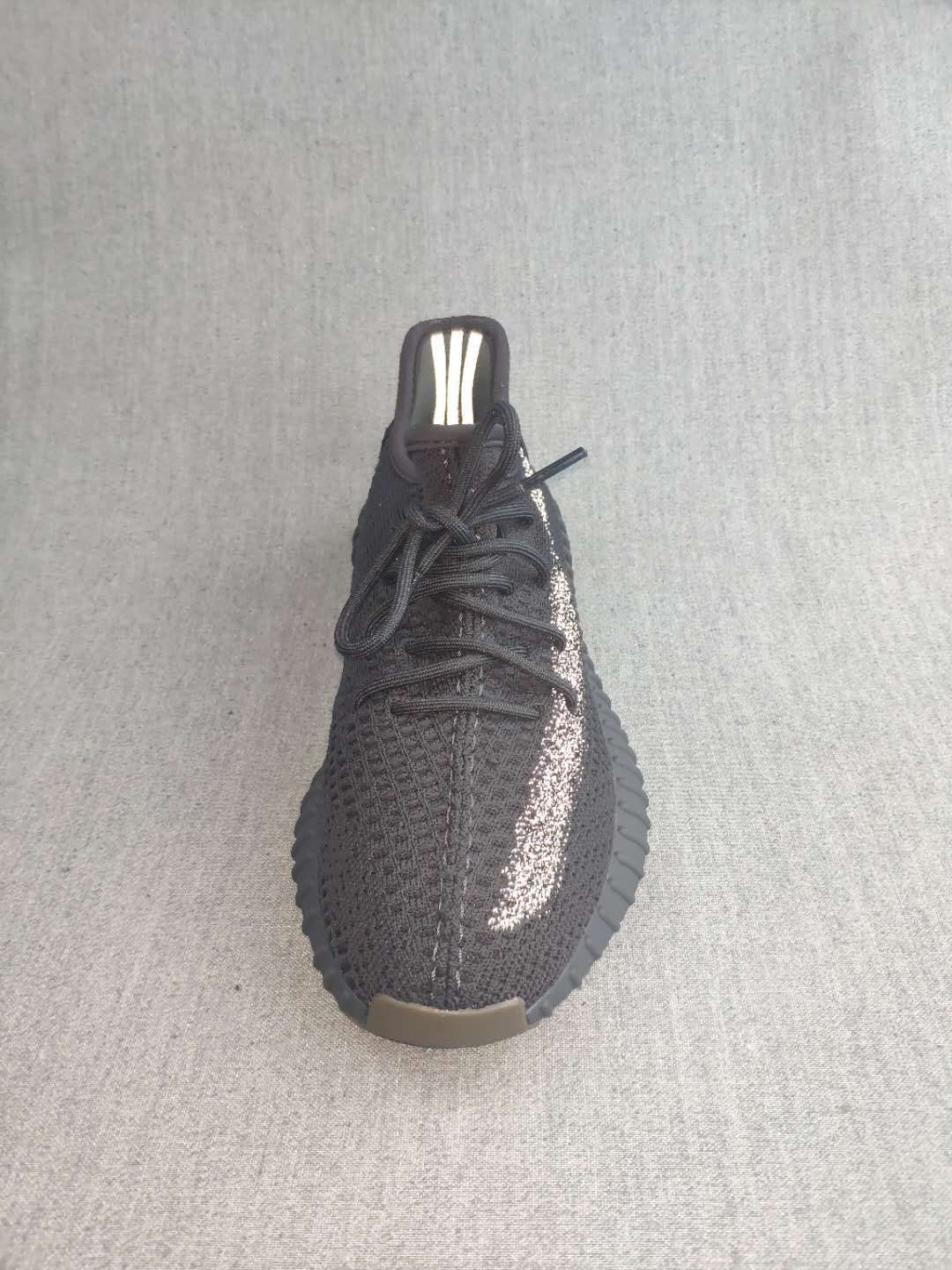 Top view of a black lace-up sneaker showing the textured upper, reflective side detail, and pull tab.