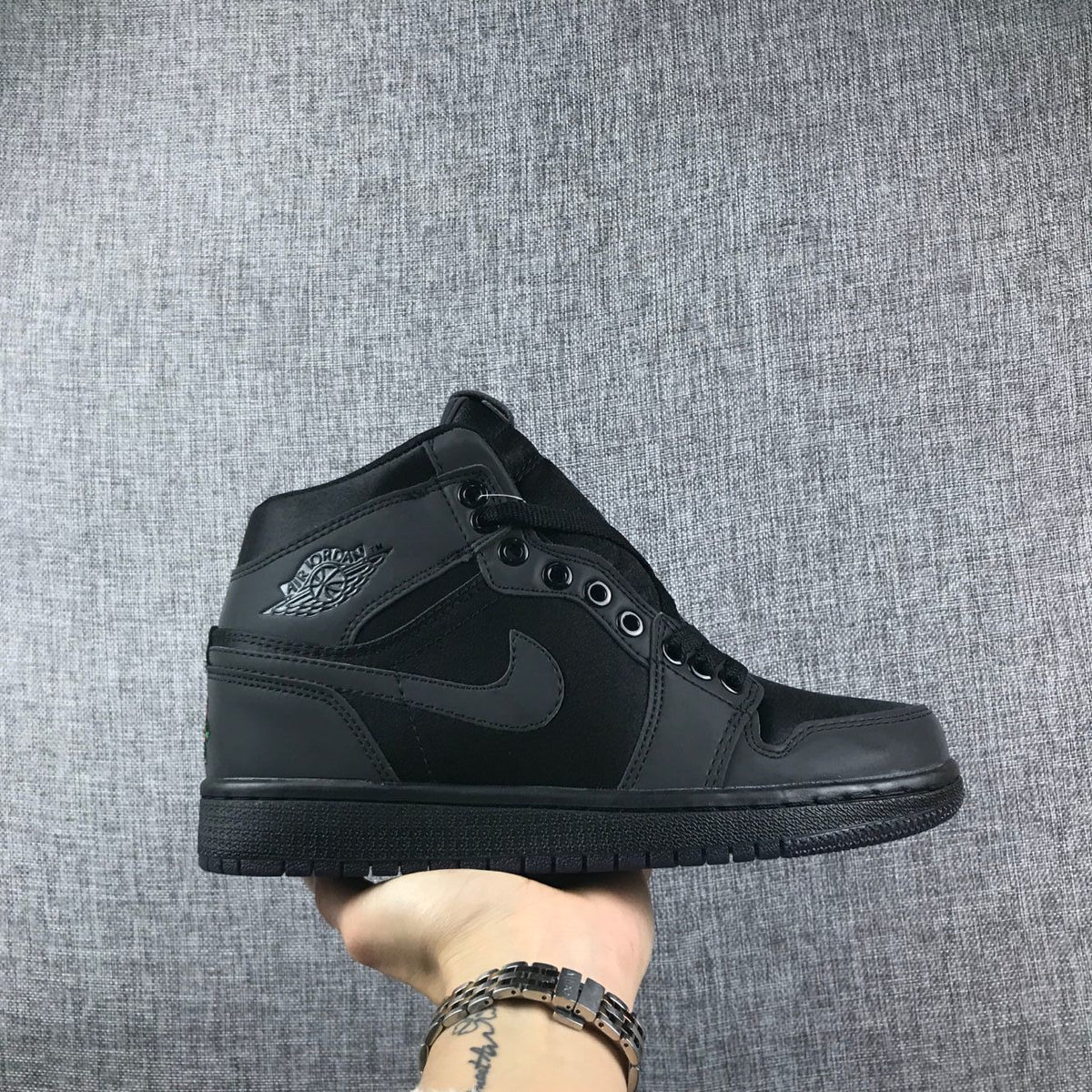 Side view of a black high-top Jordan sneaker showing tonal branding, laces, and a black rubber sole.
