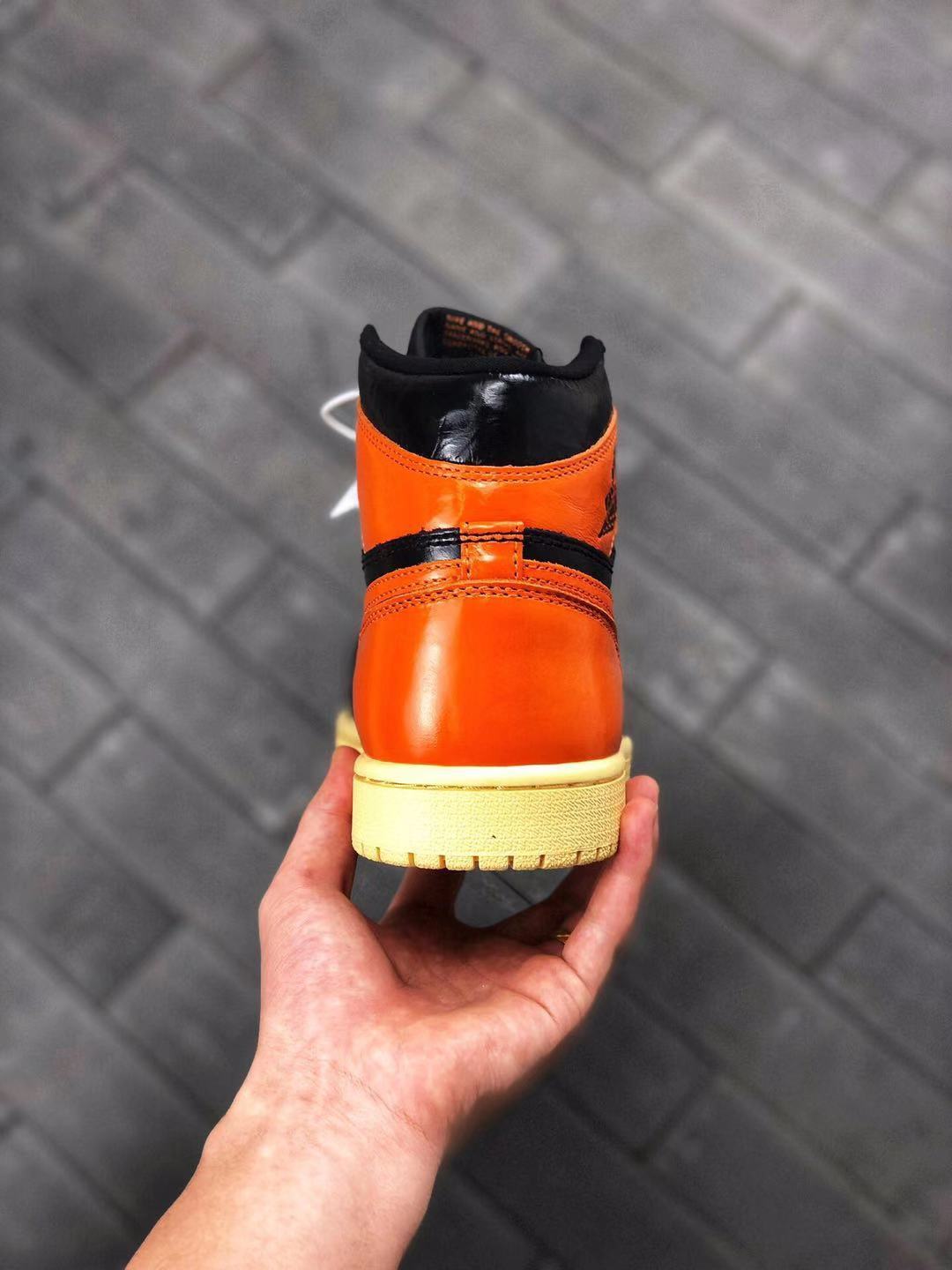 Rear close-up showing the orange heel panel, black collar, stitching, and cream-colored outsole.