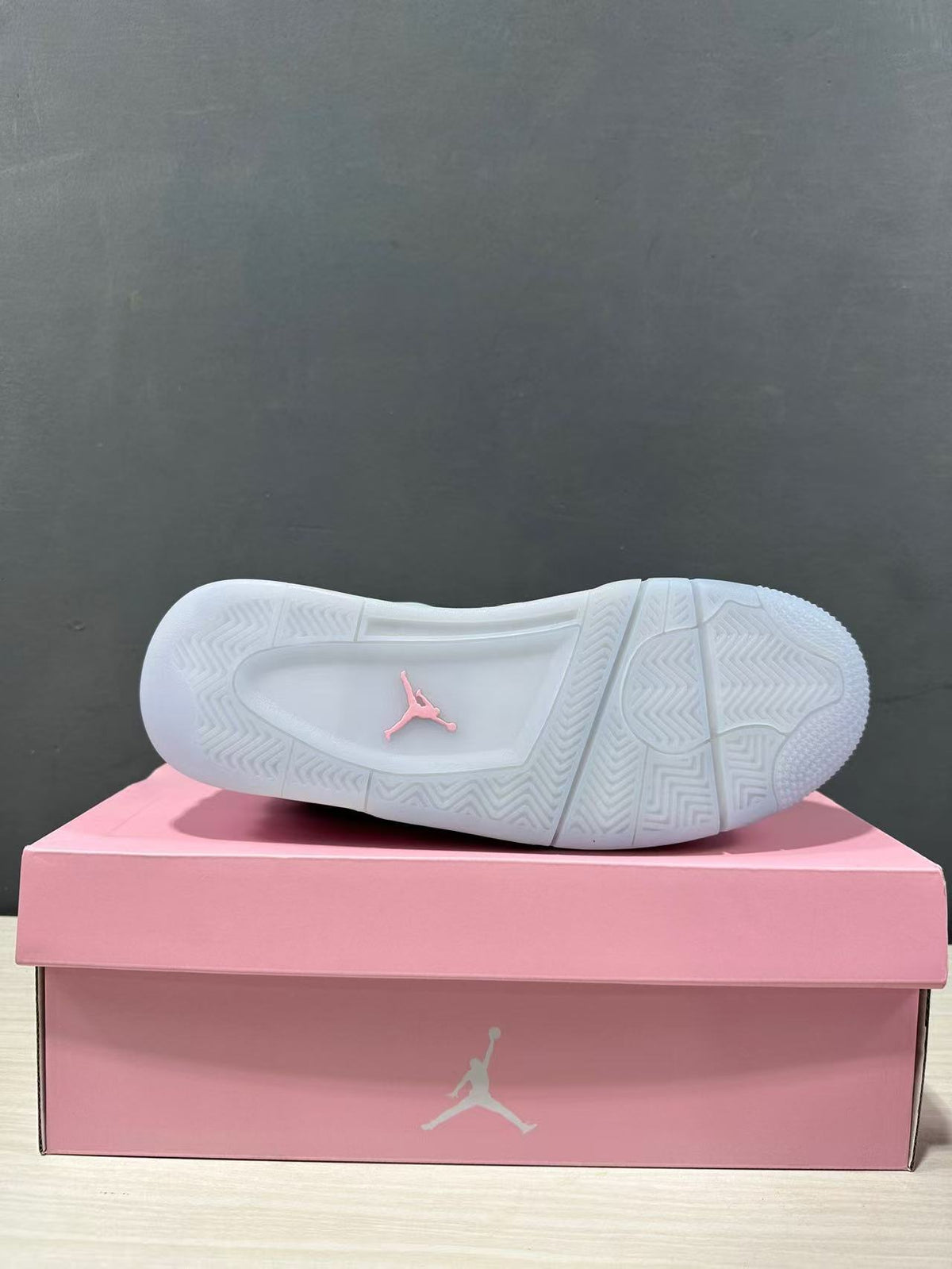 Bottom view of one sneaker showing a mostly white patterned rubber outsole with a pink Jordan logo.
