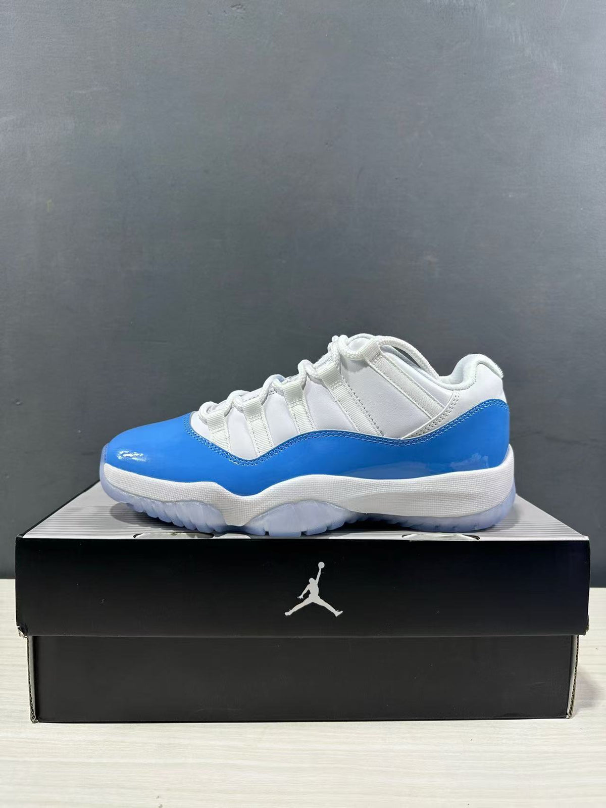 Side profile of a white and university blue low-top sneaker displayed on a black shoe box.