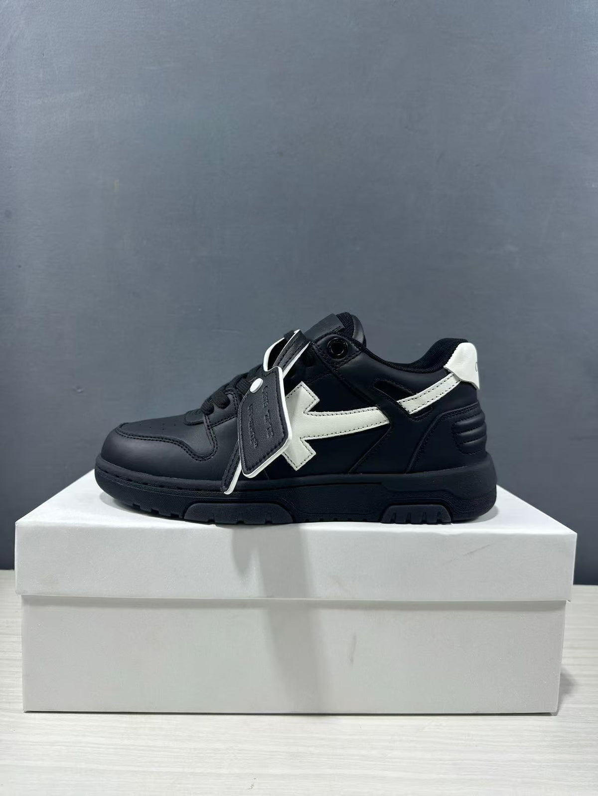 Side profile of a black and white lace-up sneaker with a white arrow detail, white heel panel, and black platform-style outsole.