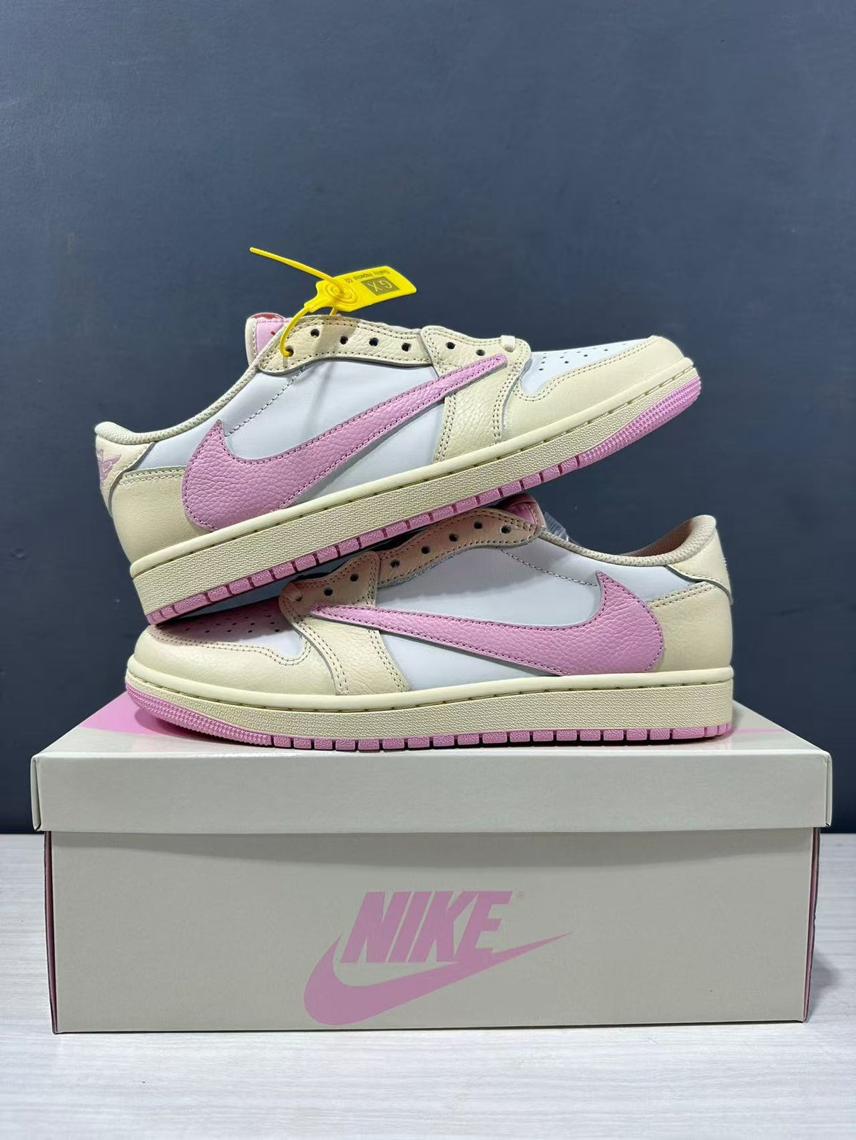 Pair of low-top sneakers stacked on a shoe box, showing the pink side branding and cream overlays.