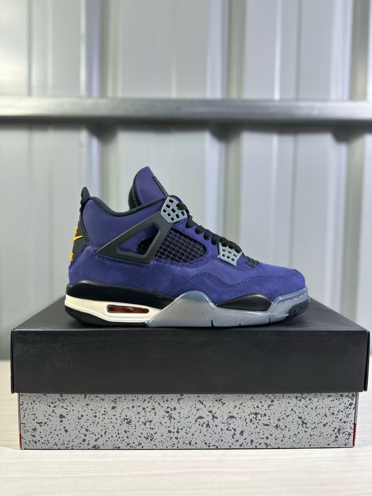 Side profile of a purple Jordan Air Jordan 4 sneaker displayed on a speckled shoebox.