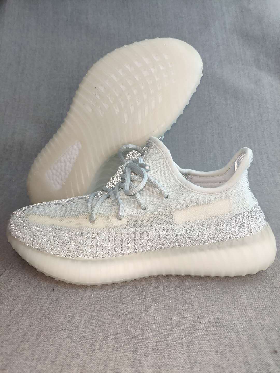 Side view of a white and silver Yeezy 350 V2-style sneaker with reflective-looking detailing and a translucent ribbed sole.