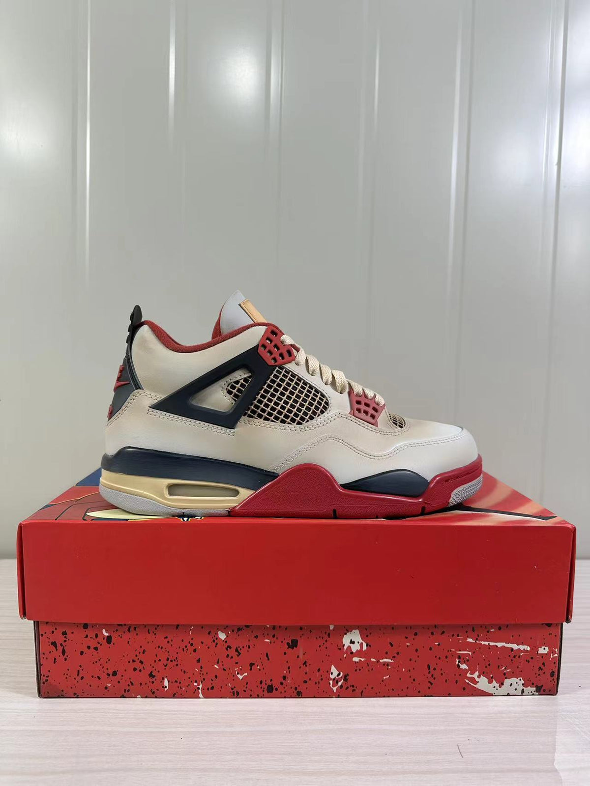 Side profile of an off-white Jordan Air Jordan 4 Retro sneaker with red trim, dark navy overlays, and a visible heel unit.