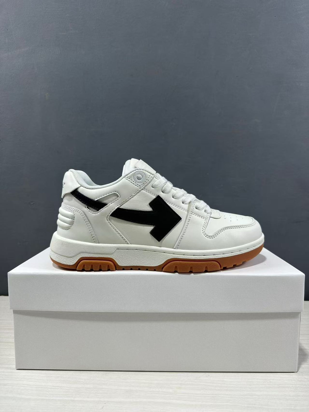 Side profile of the white low-top sneaker with black arrow detailing and a gum-colored outsole.