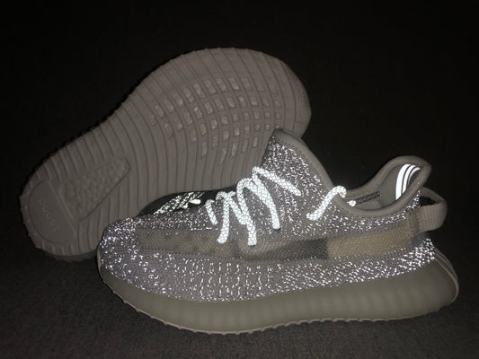 Pair of white and grey Yeezy-style sneakers shown from the side and outsole, with reflective-looking details under flash.
