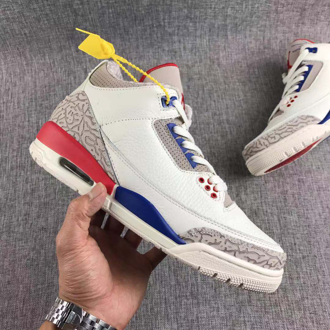 Single sneaker shown in side profile with a white upper, patterned grey toe and heel panels, blue accents, and a red heel section.